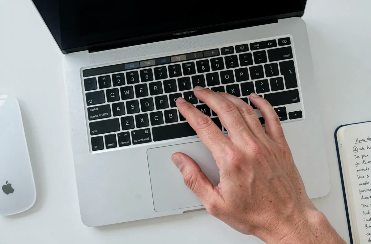 Gros plan du clavier Mac AZERTY avec un doigt sur la touche pour taper un point d'exclamation, vue du dessus