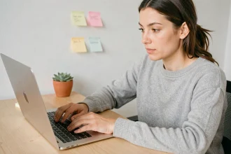 Femme cherchant comment faire un point d'exclamation sur un clavier Mac avec un MacBook Pro ouvert sur un bureau en bois